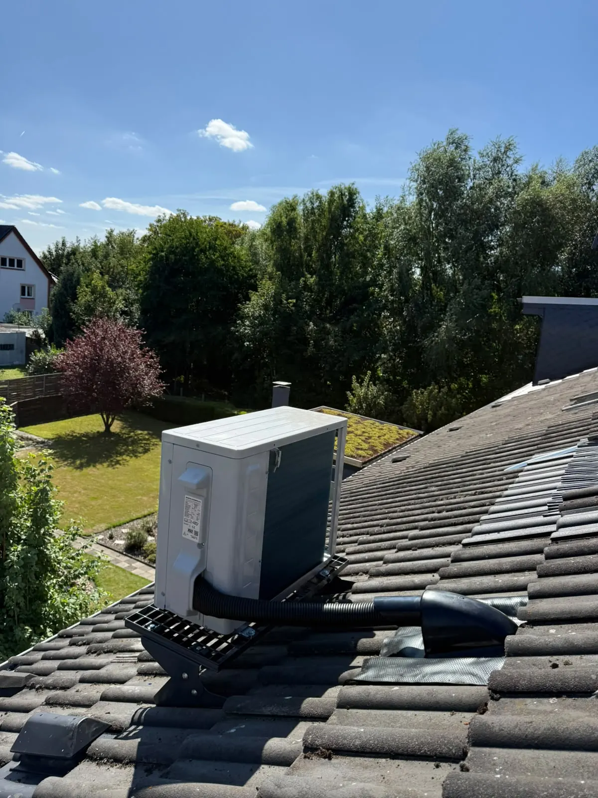 Daikin-Außengerät auf einer Dachkonsole, die Leitung führt durch einen Lüfterziegel ins Haus