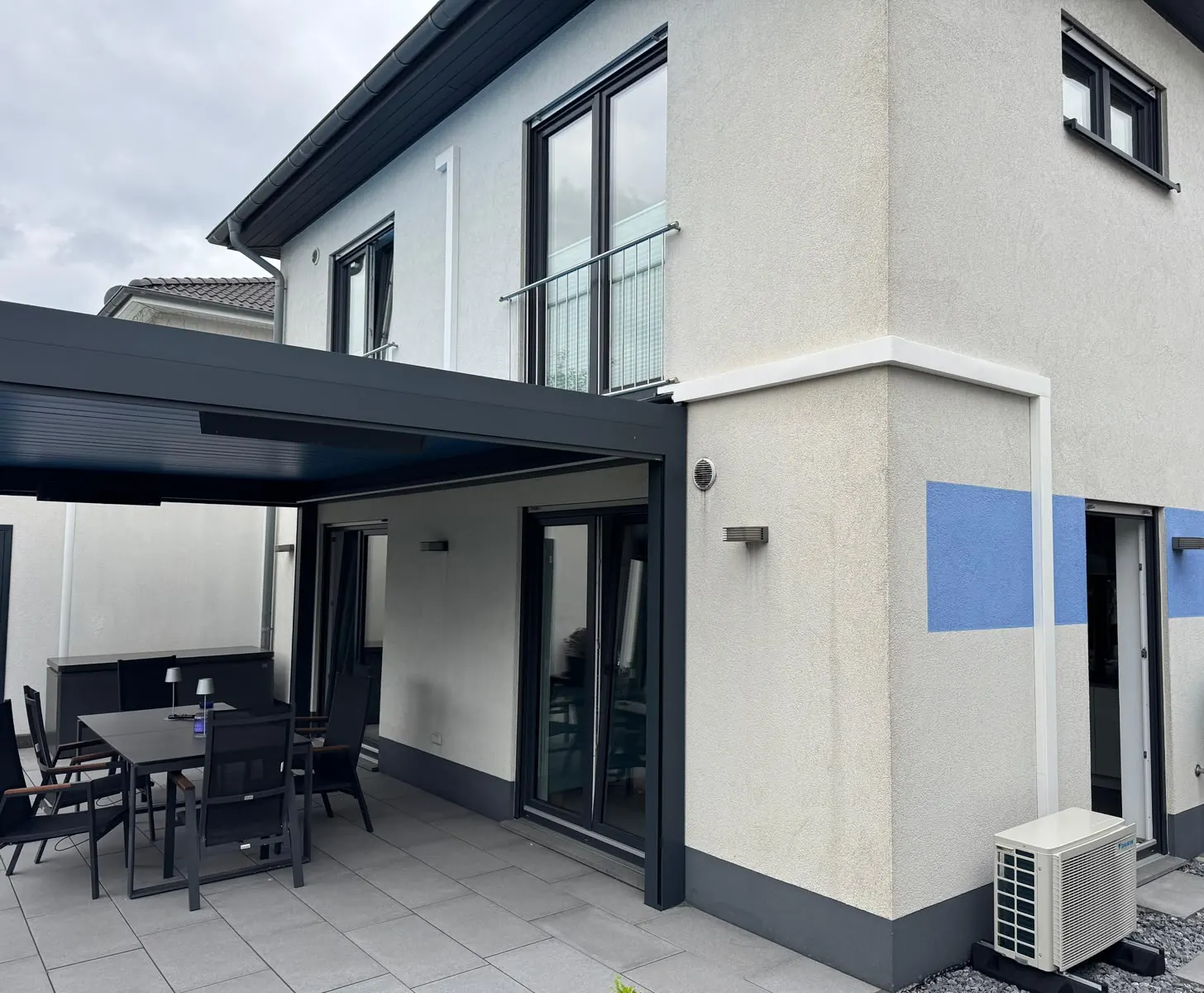 Von DBO montiertes Außengerät am Sockel eines Neubaus, daneben die überdachte Terrasse